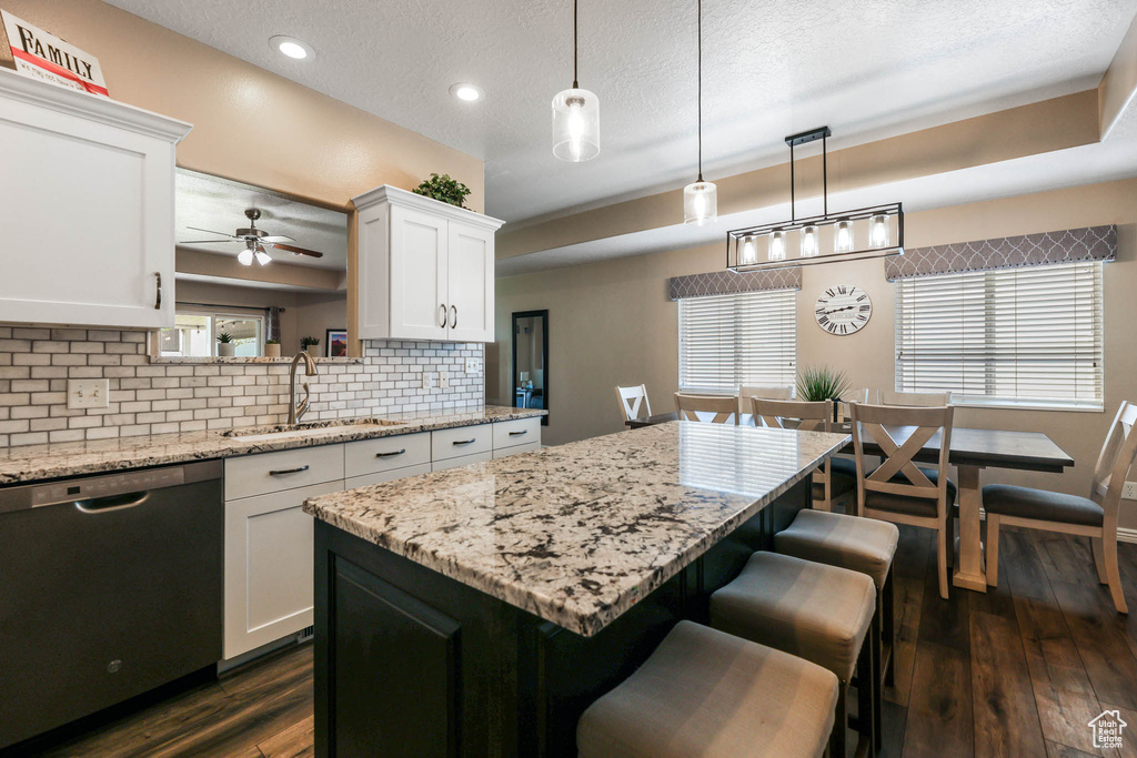 Kitchen with stainless steel dishwasher, decorative backsplash, a breakfast bar area, white cabinets, and ceiling fan