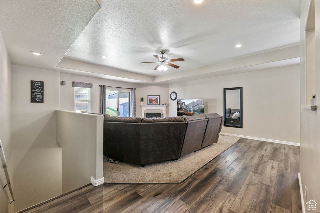 Living room with wood finished floors, ceiling fan, a textured ceiling, a raised ceiling, and a fireplace