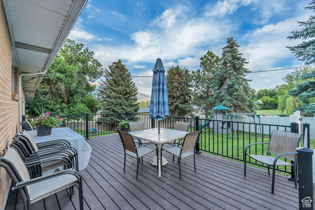 Wooden terrace with outdoor dining area, a playground, and a fenced backyard