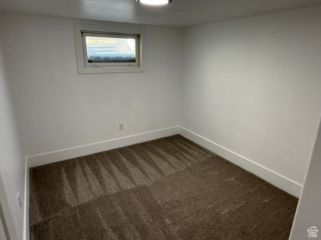 Unfurnished room featuring dark colored carpet and baseboards