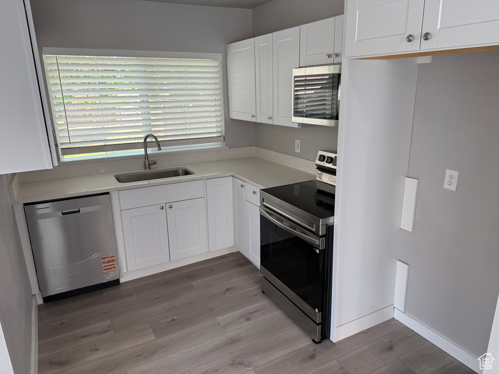 Kitchen with appliances with stainless steel finishes, light wood finished floors, white cabinets, and light countertops