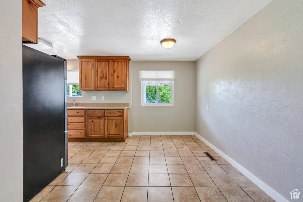 Kitchen featuring freestanding refrigerator, plenty of natural light, light countertops, brown cabinetry, and a textured ceiling
