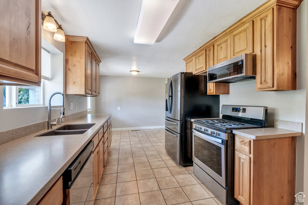 Kitchen with stainless steel appliances, light tile patterned floors, light countertops, and light brown cabinets