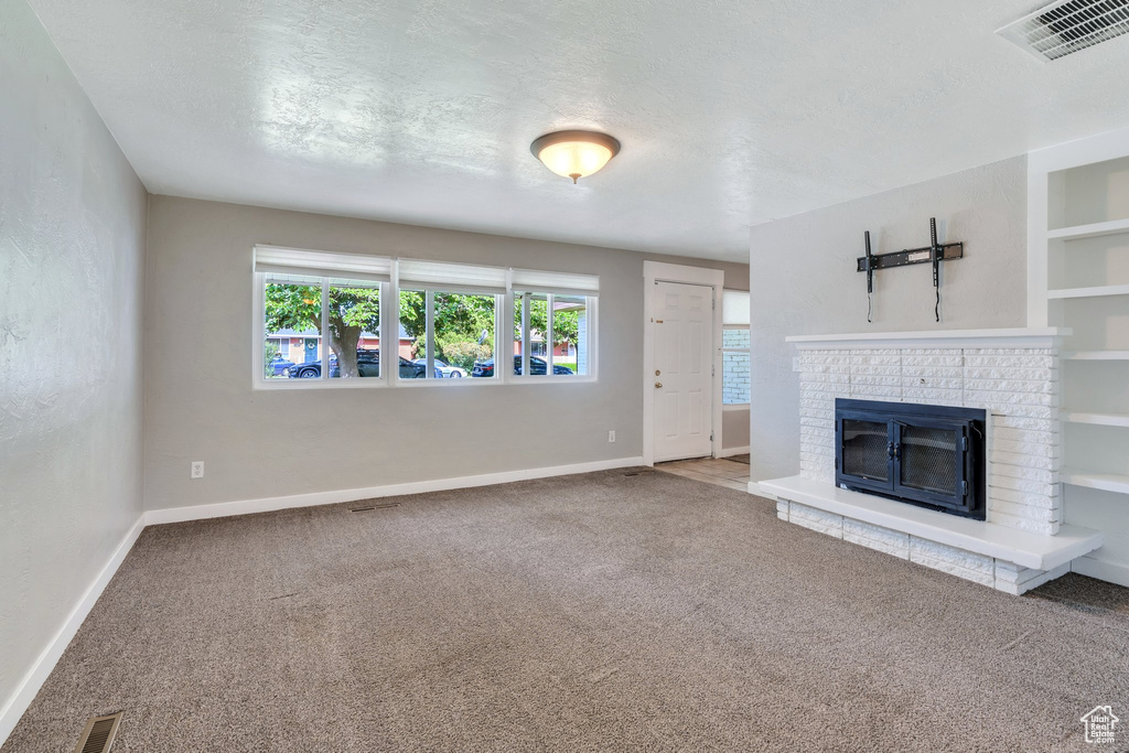 Unfurnished living room featuring carpet flooring and a brick fireplace