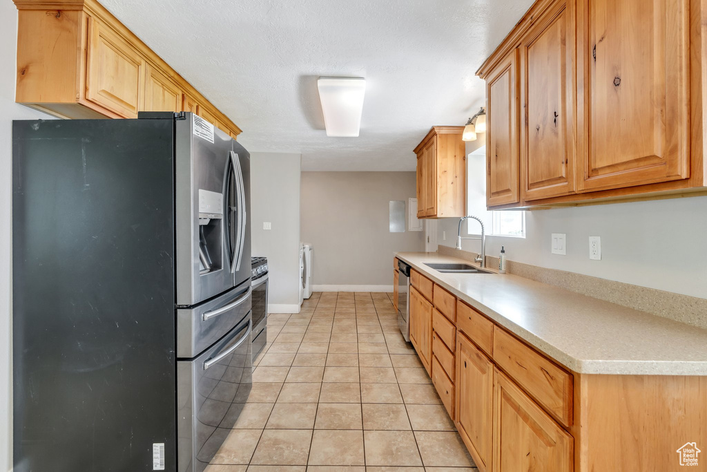 Kitchen featuring appliances with stainless steel finishes, washer / dryer, light tile patterned floors, and light countertops