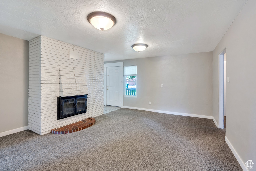Unfurnished living room with carpet floors, a textured ceiling, and a fireplace