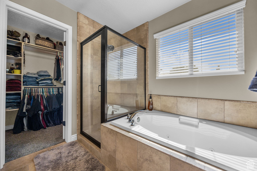 Full bath featuring a jetted tub, a stall shower, a walk in closet, and tile patterned flooring