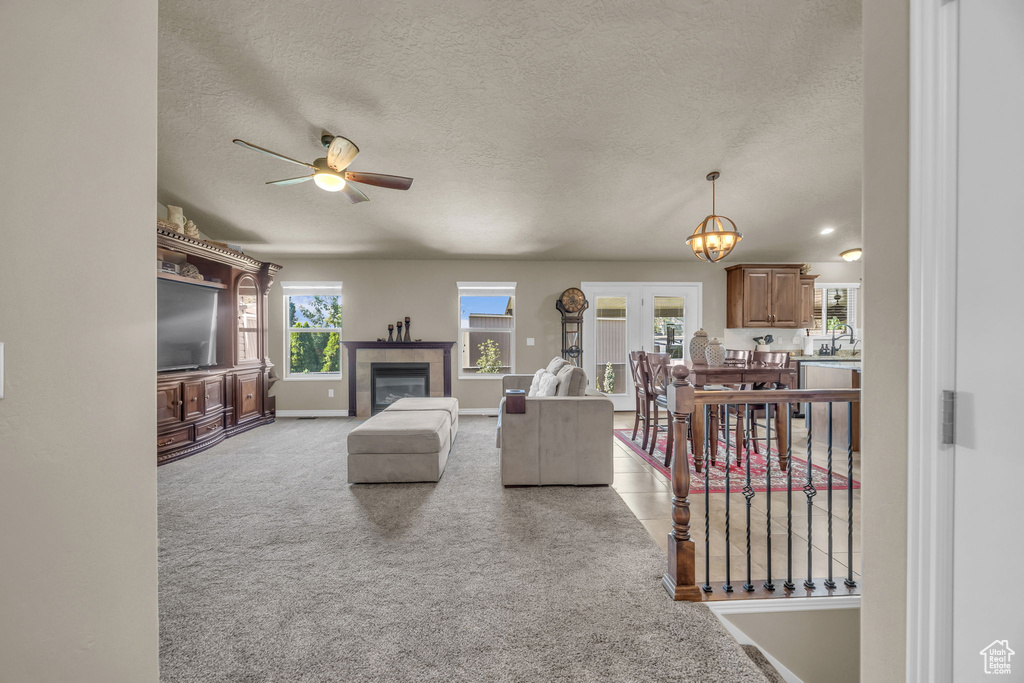 Living area with a ceiling fan, a textured ceiling, a fireplace, and carpet floors