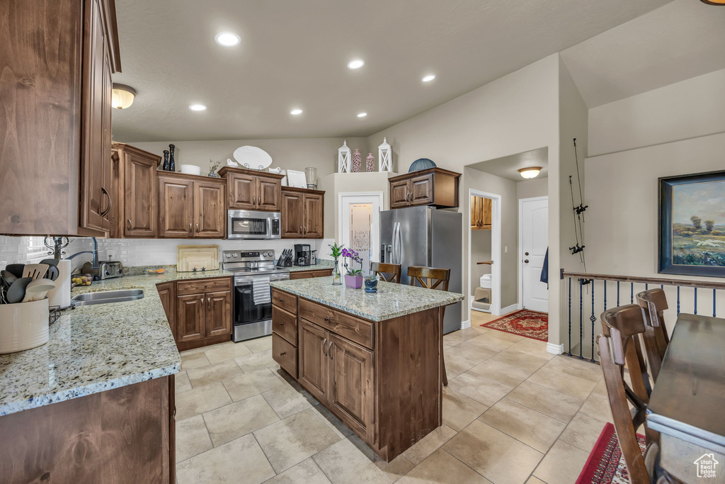 Kitchen with stainless steel appliances, vaulted ceiling, light stone counters, a kitchen island, and recessed lighting
