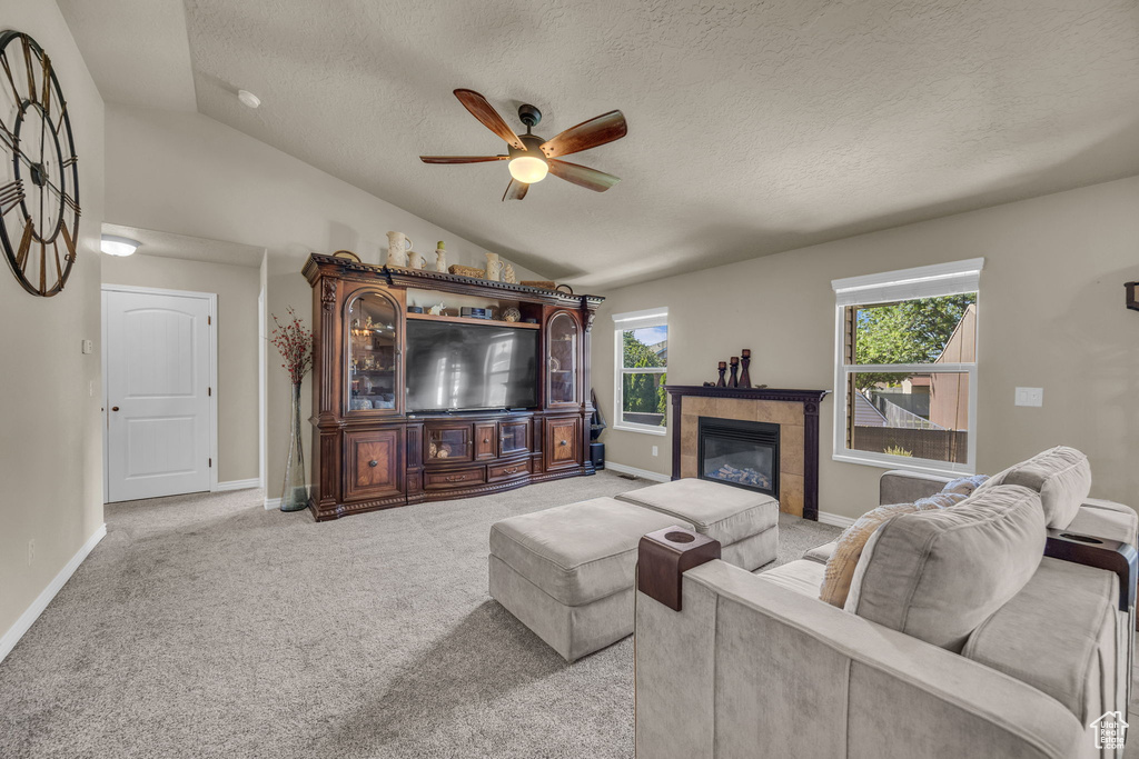 Living area with vaulted ceiling, ceiling fan, a textured ceiling, light carpet, and a fireplace