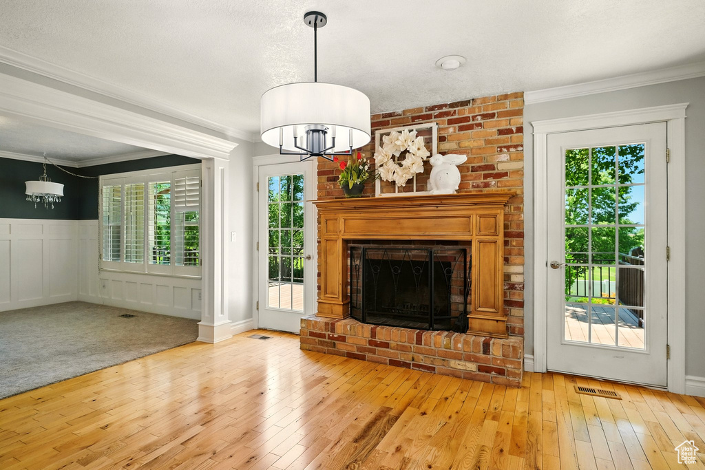 Unfurnished living room featuring a chandelier, healthy amount of natural light, light wood finished floors, crown molding, and a wainscoted wall