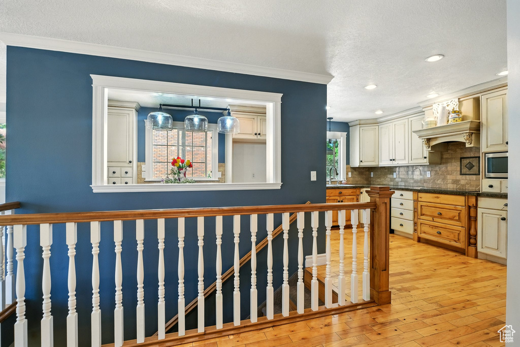 Kitchen with tasteful backsplash, stainless steel microwave, light wood finished floors, dark countertops, and ornamental molding