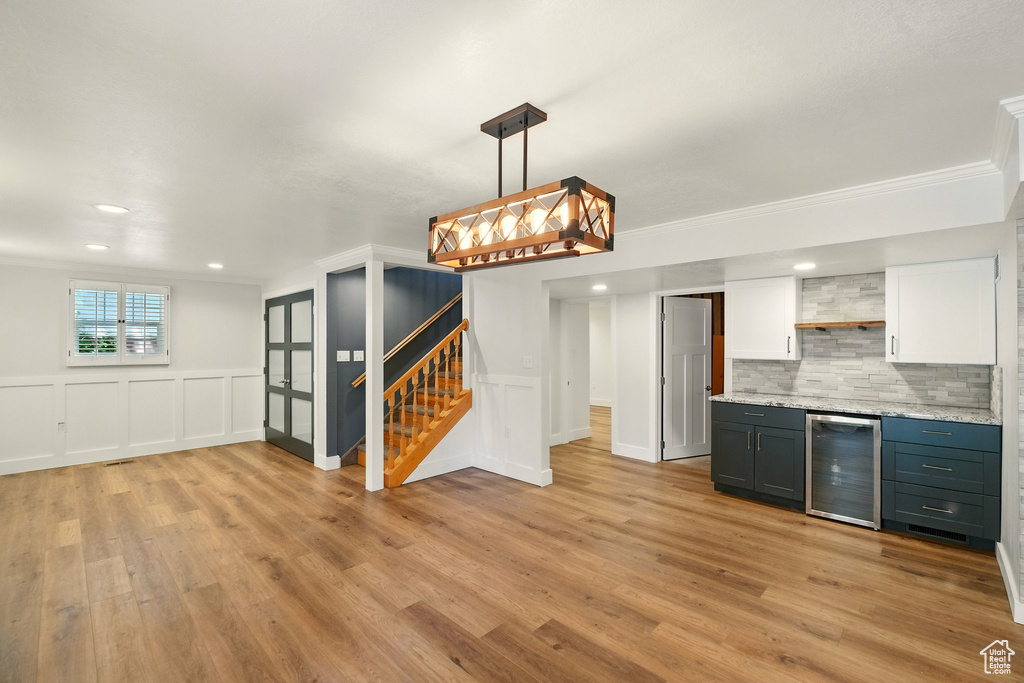 Kitchen featuring beverage cooler, open shelves, light wood-style floors, white cabinets, and ornamental molding