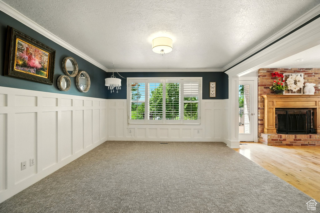 Unfurnished living room featuring healthy amount of natural light, a decorative wall, crown molding, a textured ceiling, and a fireplace