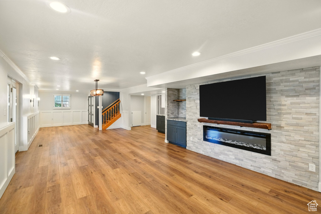 Unfurnished living room featuring ornamental molding, a fireplace, stairs, recessed lighting, and light wood-style flooring