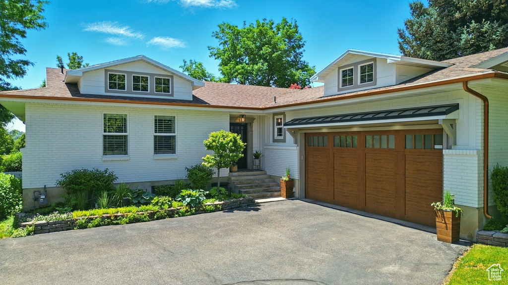 View of front of property with brick siding, driveway, an attached garage, and a shingled roof