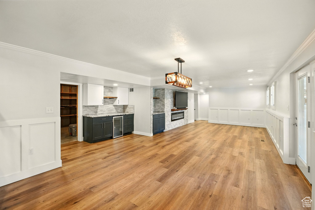 Unfurnished living room featuring wine cooler, ornamental molding, a decorative wall, light wood-style flooring, and recessed lighting
