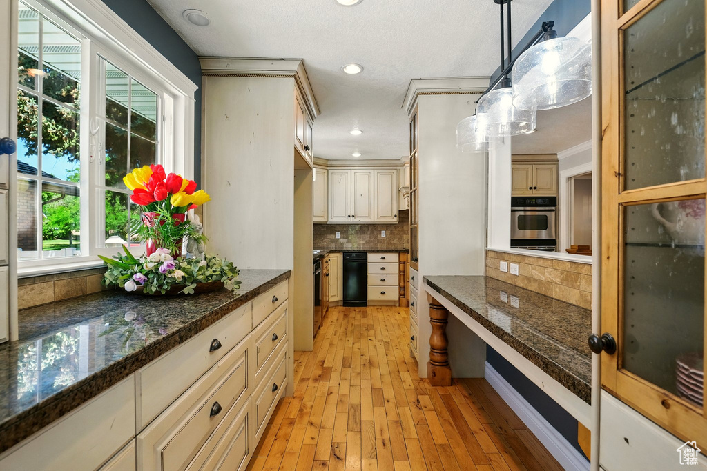 Kitchen with stainless steel oven, light wood-style flooring, decorative backsplash, cream cabinets, and hanging light fixtures