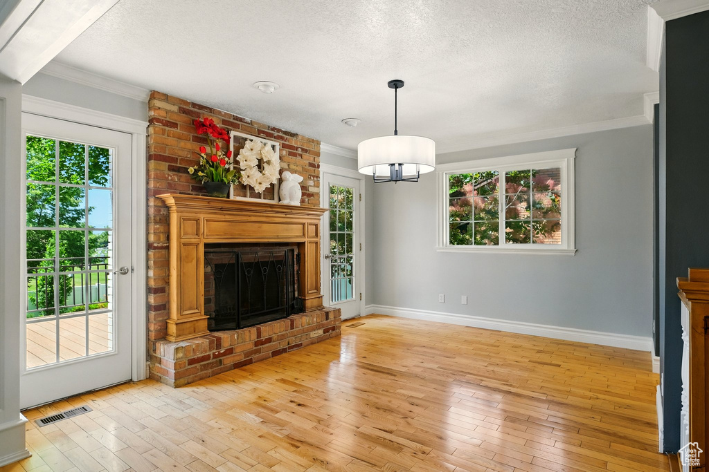 Unfurnished living room with light wood finished floors, a textured ceiling, a fireplace, crown molding, and a chandelier