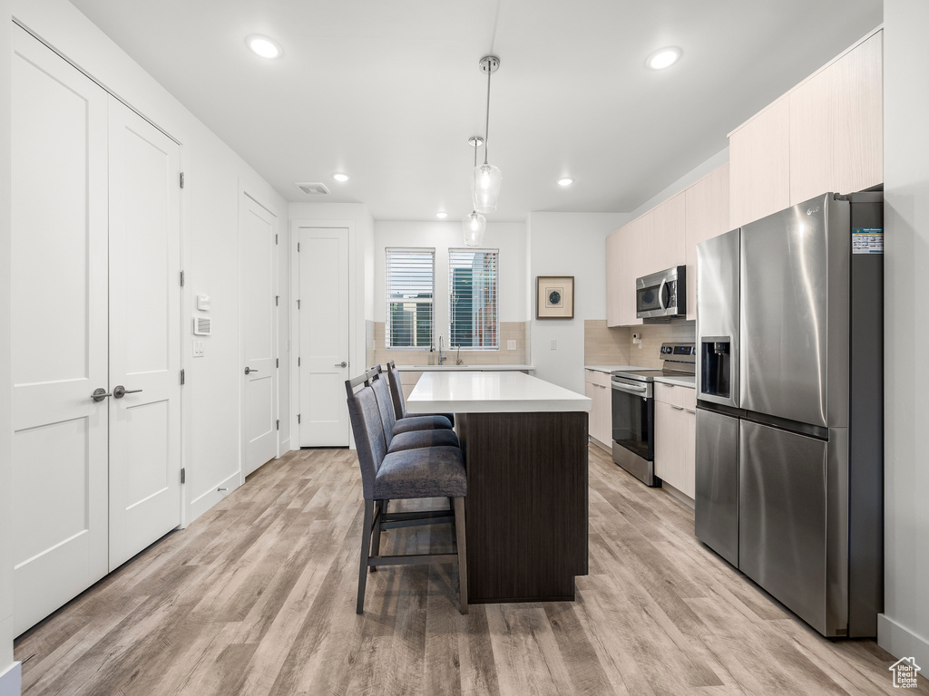Kitchen with stainless steel appliances, light countertops, a kitchen breakfast bar, a kitchen island, and light wood-type flooring