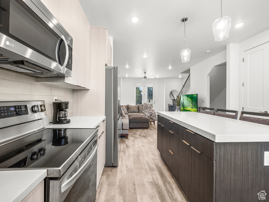 Kitchen with appliances with stainless steel finishes, open floor plan, light wood-type flooring, dark brown cabinets, and light countertops