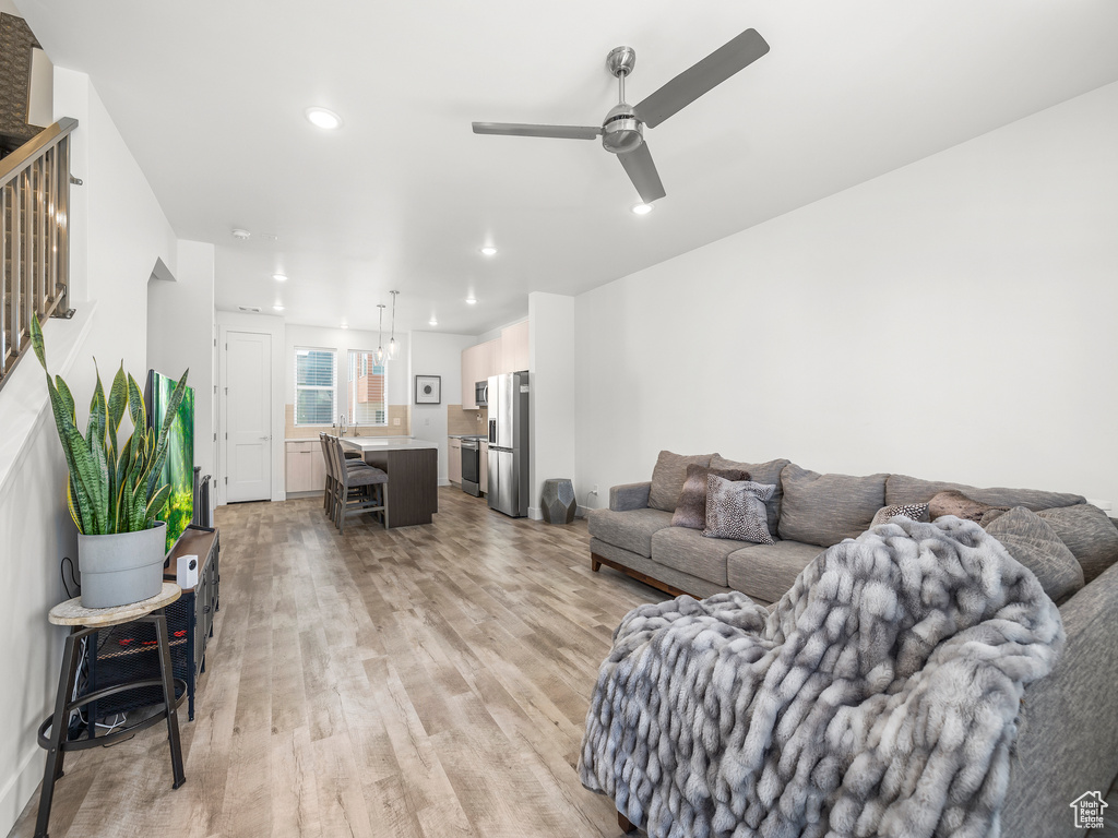 Living room with light wood-style floors, ceiling fan, recessed lighting, and stairs