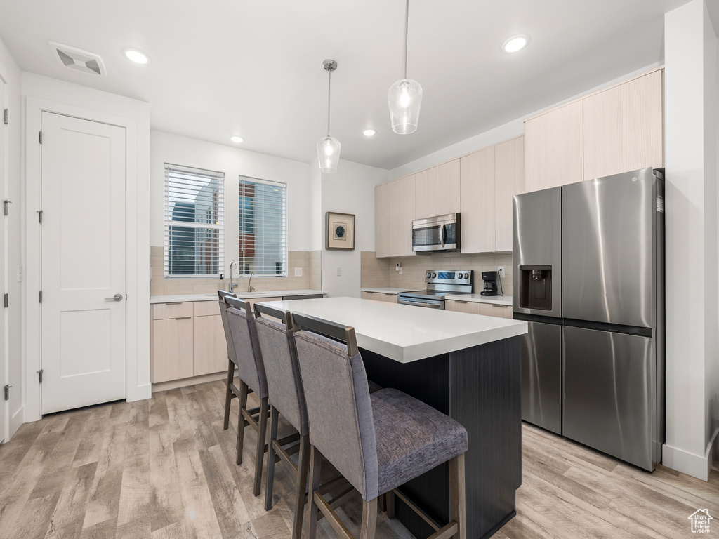 Kitchen with appliances with stainless steel finishes, light countertops, a kitchen island, tasteful backsplash, and modern cabinets