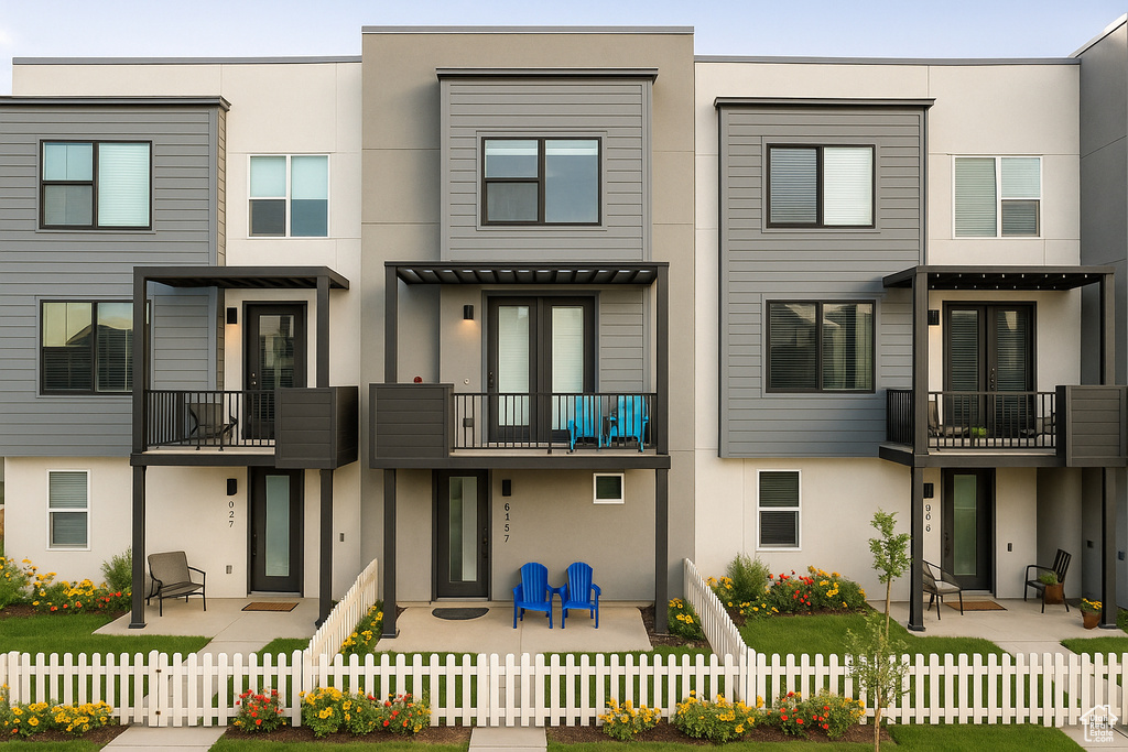 View of front facade with stucco siding, a balcony, a fenced front yard, and a patio