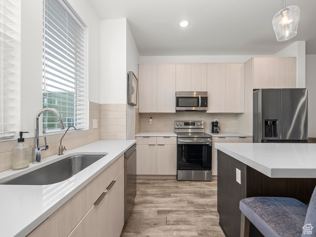 Kitchen featuring appliances with stainless steel finishes, light brown cabinetry, light countertops, light wood-type flooring, and recessed lighting