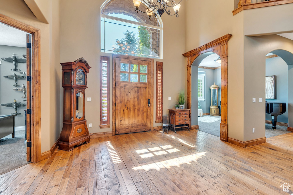 Foyer entrance with arched walkways, a high ceiling, light wood finished floors, healthy amount of natural light, and a chandelier