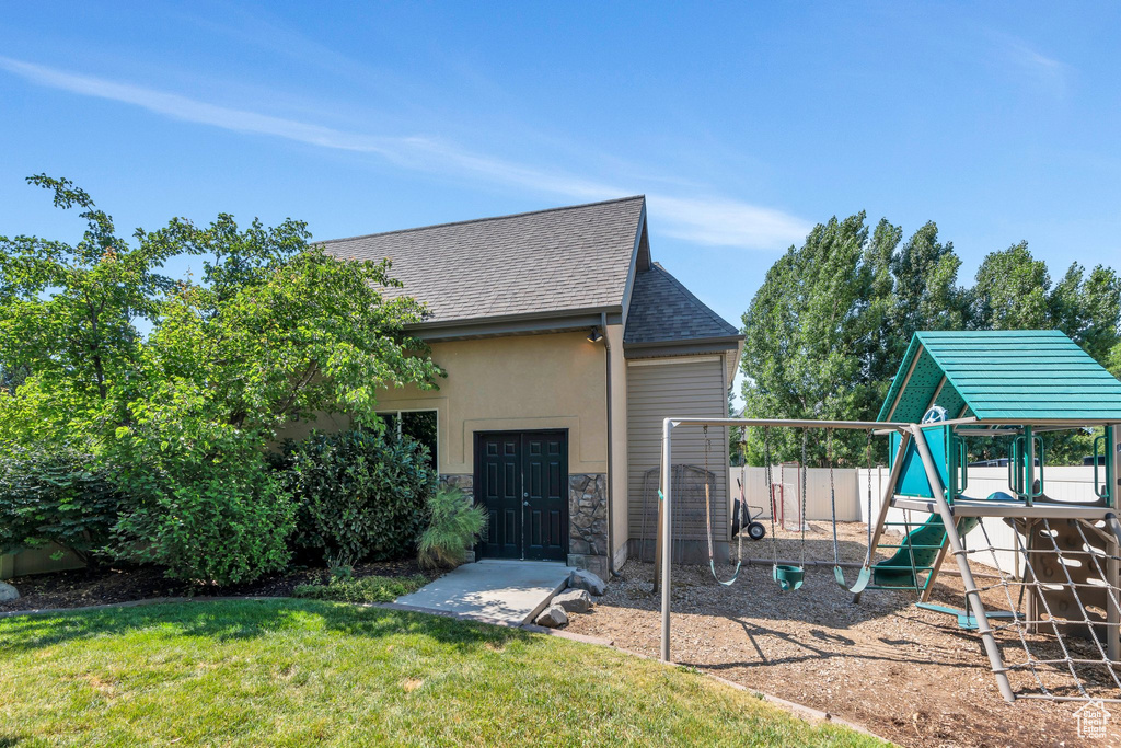 Rear view of property with a playground, stone siding, a shingled roof, and an attached garage