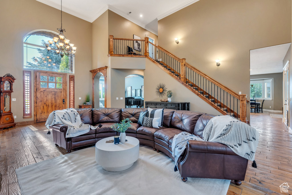 Living room with stairs, a chandelier, hardwood / wood-style floors, crown molding, and arched walkways
