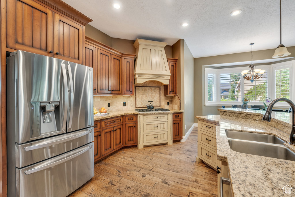 Kitchen featuring stainless steel appliances, premium range hood, light wood finished floors, recessed lighting, and decorative backsplash