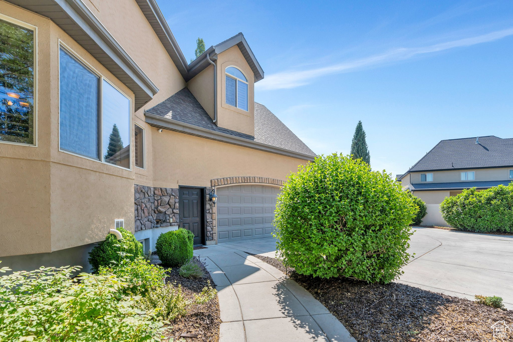 View of side of property featuring stucco siding, concrete driveway, stone siding, roof with shingles, and a garage