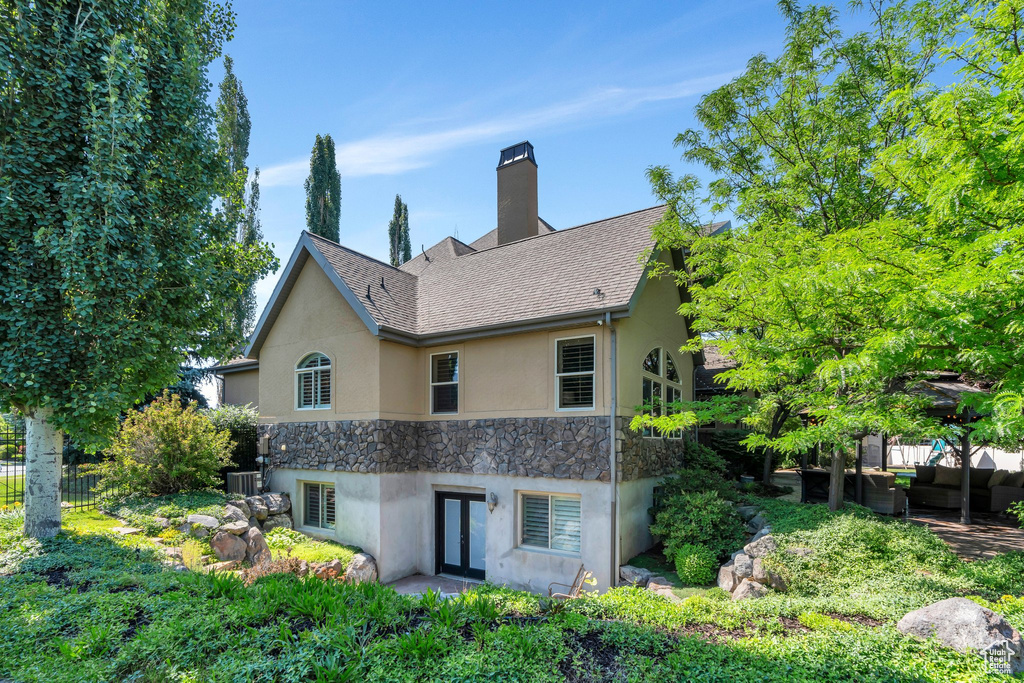 Back of house featuring stucco siding, stone siding, french doors, and a chimney