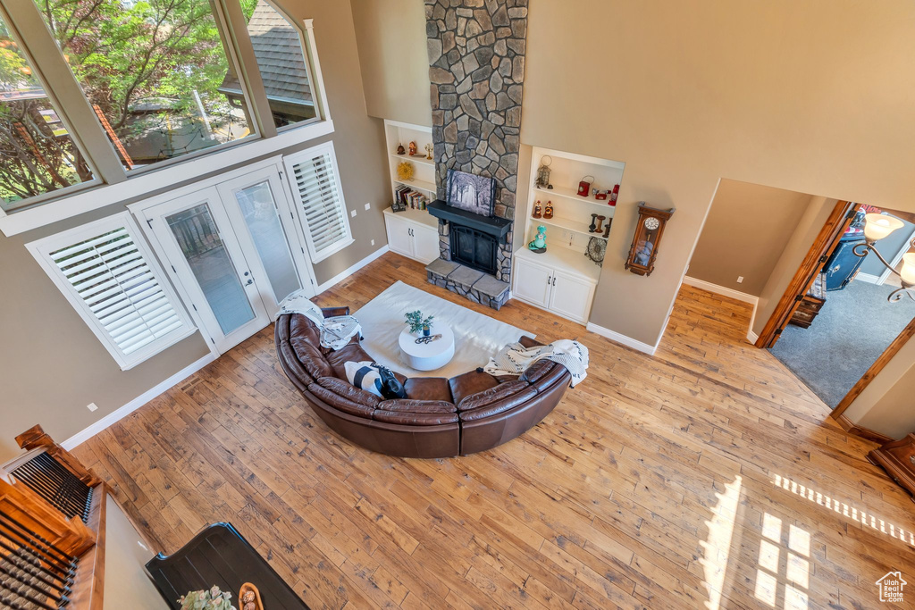 Living room featuring a towering ceiling, wood-type flooring, healthy amount of natural light, built in shelves, and a large fireplace