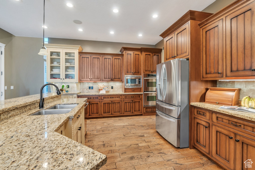 Kitchen with appliances with stainless steel finishes, brown cabinets, light wood finished floors, tasteful backsplash, and recessed lighting