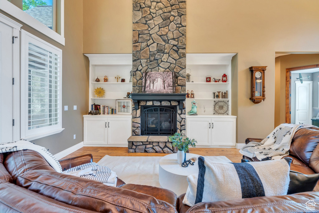 Living room featuring a stone fireplace, light wood-style floors, a towering ceiling, and built in shelves