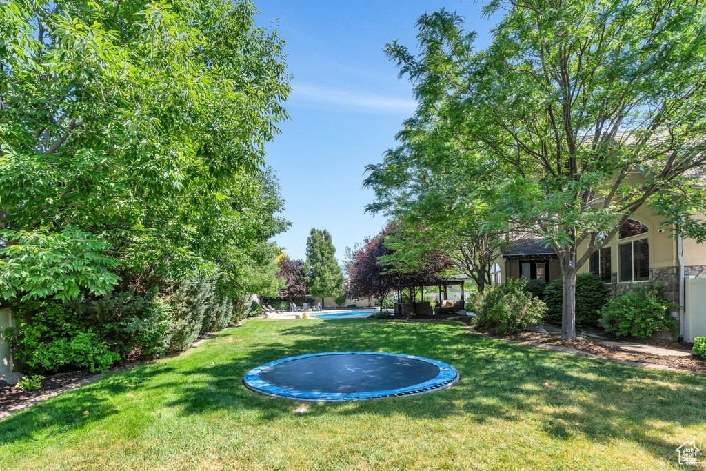 View of grassy yard featuring a trampoline, a gazebo, and an outdoor pool