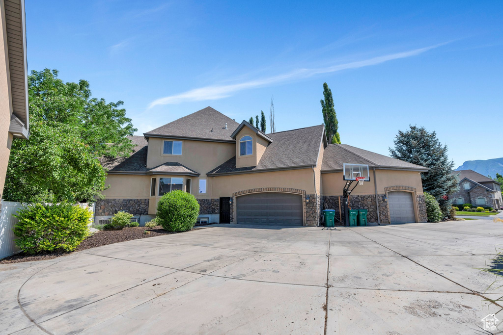 Traditional home featuring stone siding, stucco siding, an attached garage, and concrete driveway
