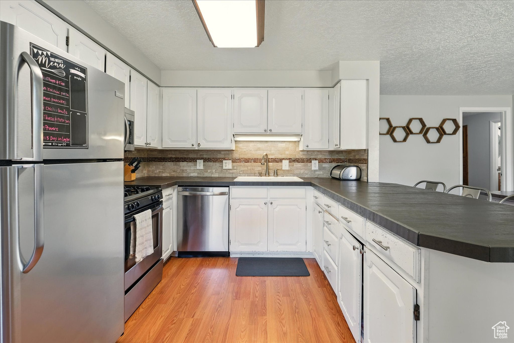 Kitchen with appliances with stainless steel finishes, a peninsula, dark countertops, a textured ceiling, and light wood-style floors
