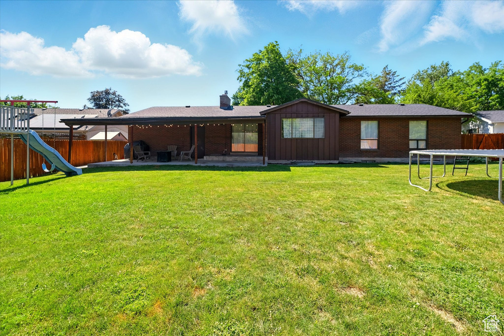 Rear view of house featuring a trampoline, a fenced backyard, a patio, brick siding, and a chimney