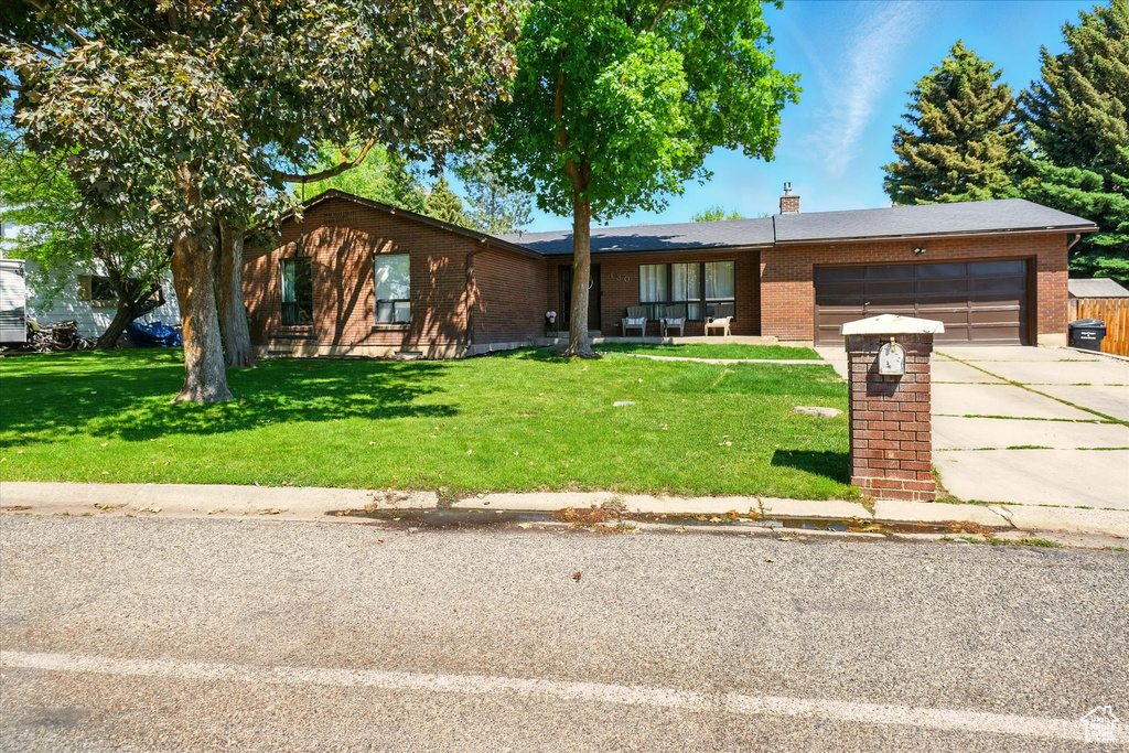 Ranch-style house featuring an attached garage, brick siding, concrete driveway, a front yard, and a chimney