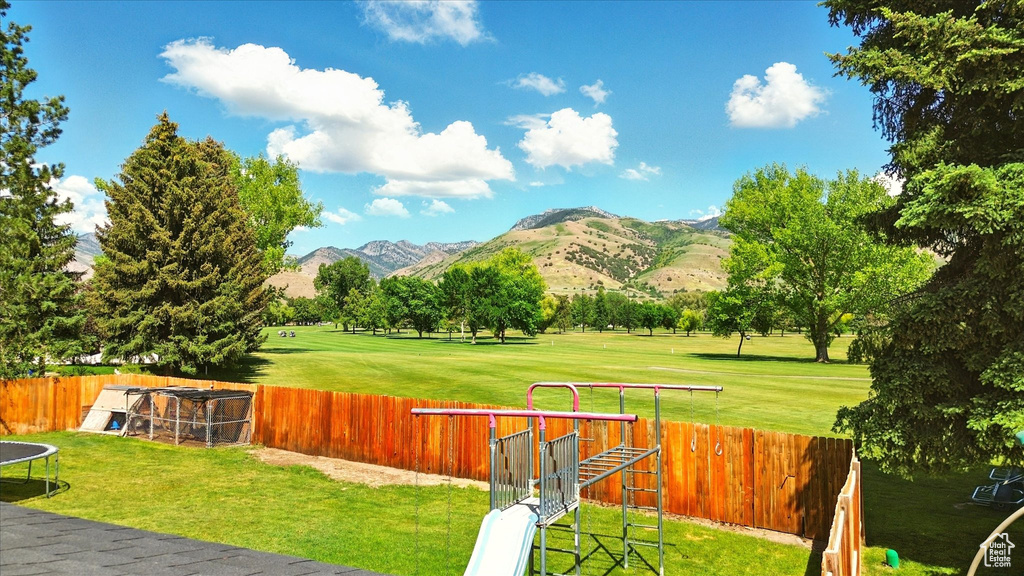 Fenced backyard with a mountain view, a trampoline, golf course view, and a playground