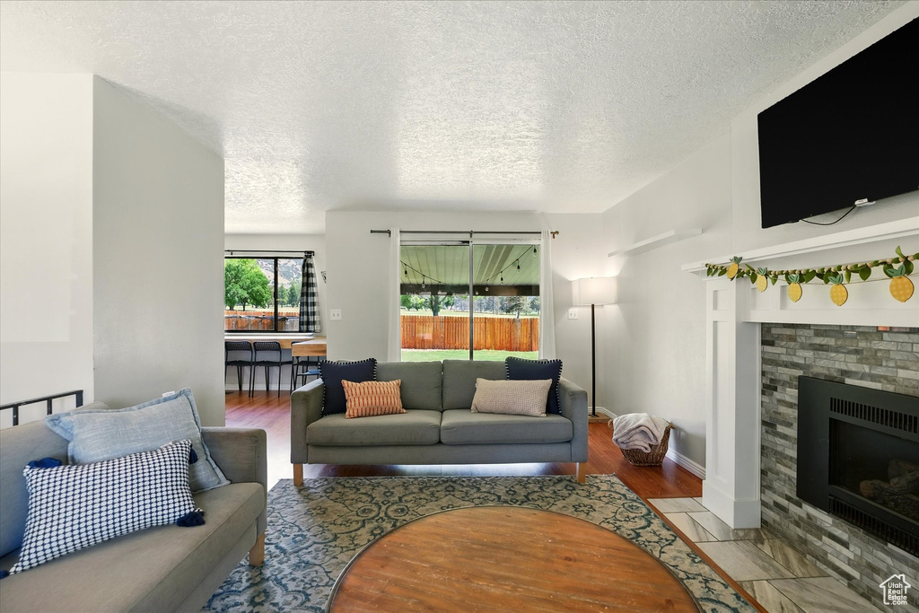 Living room with a textured ceiling, a fireplace with flush hearth, and wood finished floors