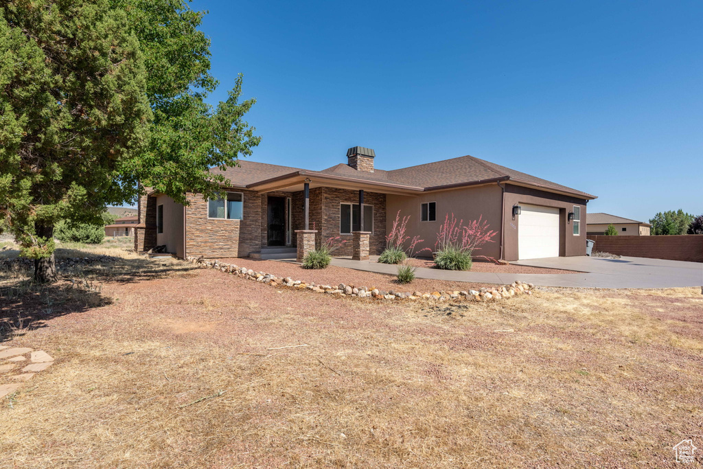 Ranch-style house with concrete driveway, a chimney, a garage, stucco siding, and stone siding