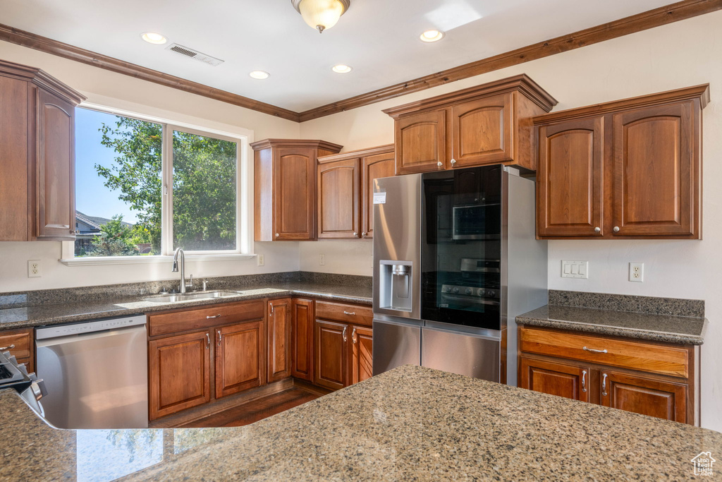 Kitchen with stainless steel appliances, crown molding, dark stone countertops, brown cabinets, and recessed lighting