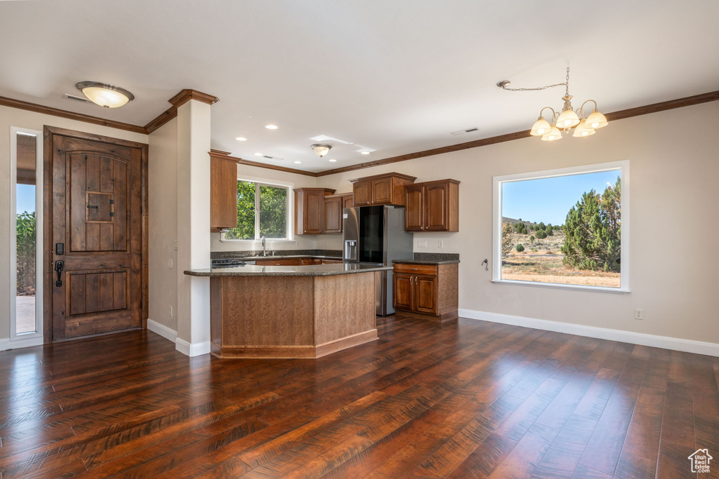 Kitchen featuring stainless steel refrigerator with ice dispenser, ornamental molding, a chandelier, dark wood-style flooring, and a peninsula