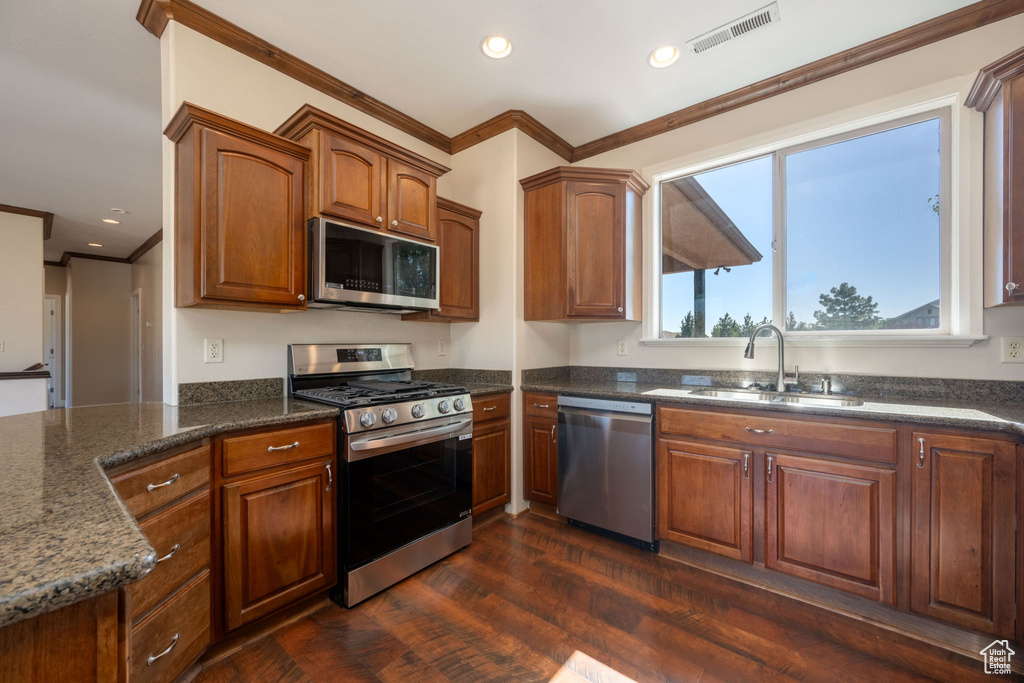 Kitchen with appliances with stainless steel finishes, ornamental molding, dark wood-style flooring, recessed lighting, and dark stone countertops