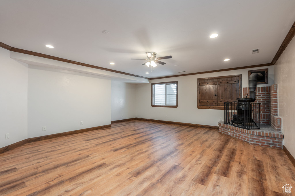 Unfurnished living room featuring a ceiling fan, a wood stove, recessed lighting, crown molding, and wood finished floors